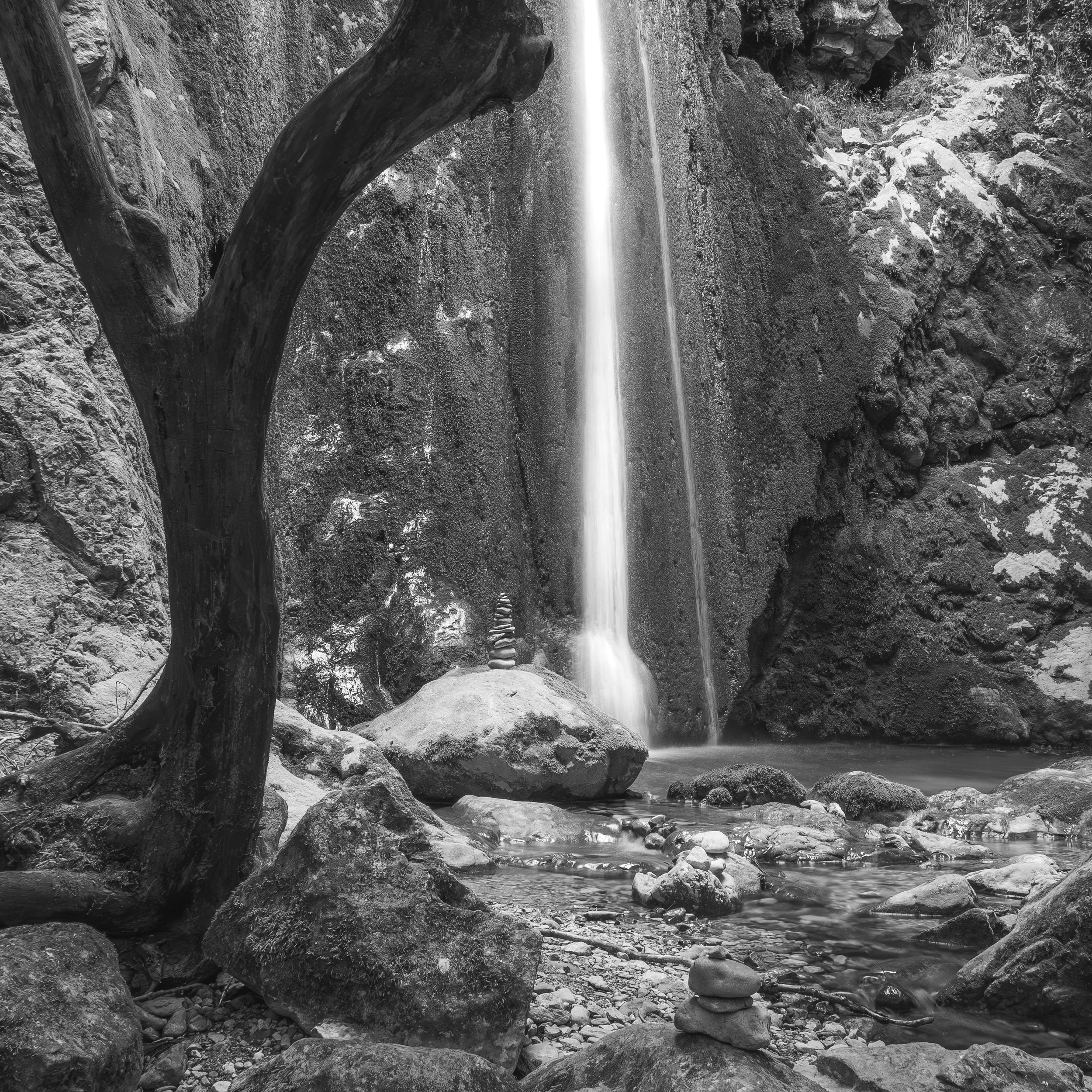 Une cascade dans un environnement rocheux, en noir et blanc, avec de l'eau tombant d'une hauteur sur des rochers en bas.