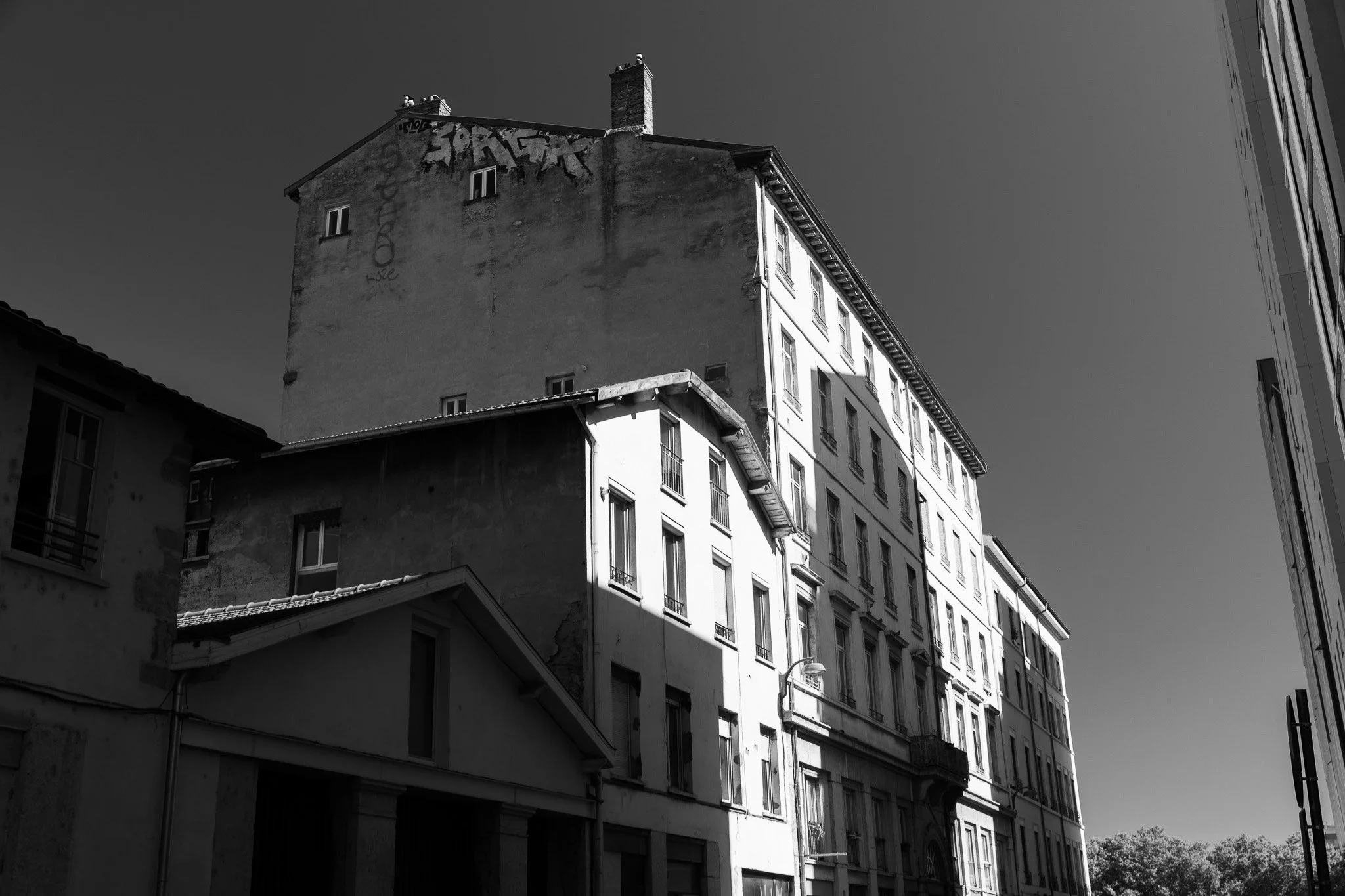 Bâtiments résidentiels en pierre avec plusieurs fenêtres sous un ciel clair, en noir et blanc.