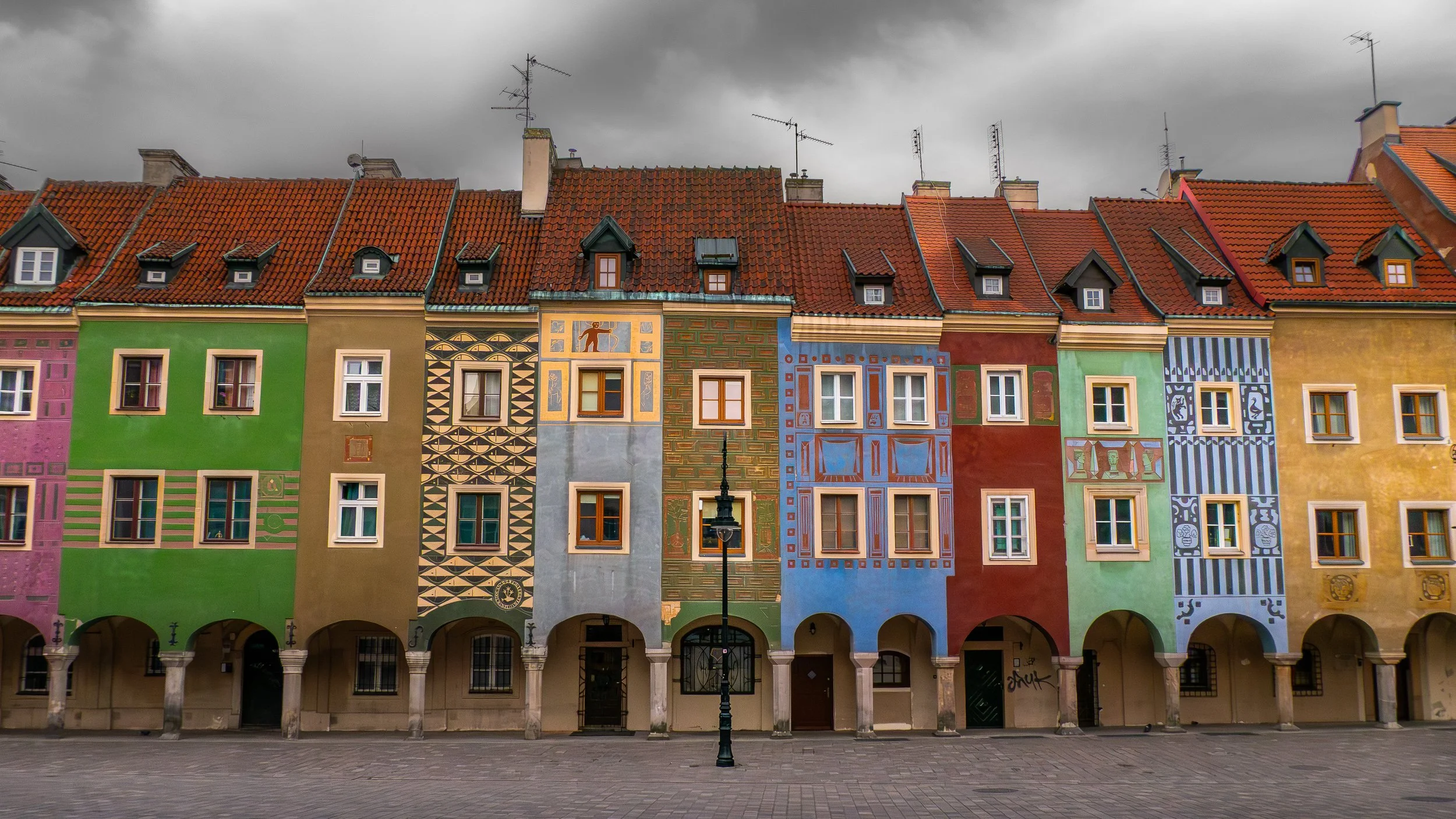 Une rangée de bâtiments colorés avec des façades ornées de motifs artistiques, au-dessus des toits en tuiles rouges sous un ciel nuageux.
