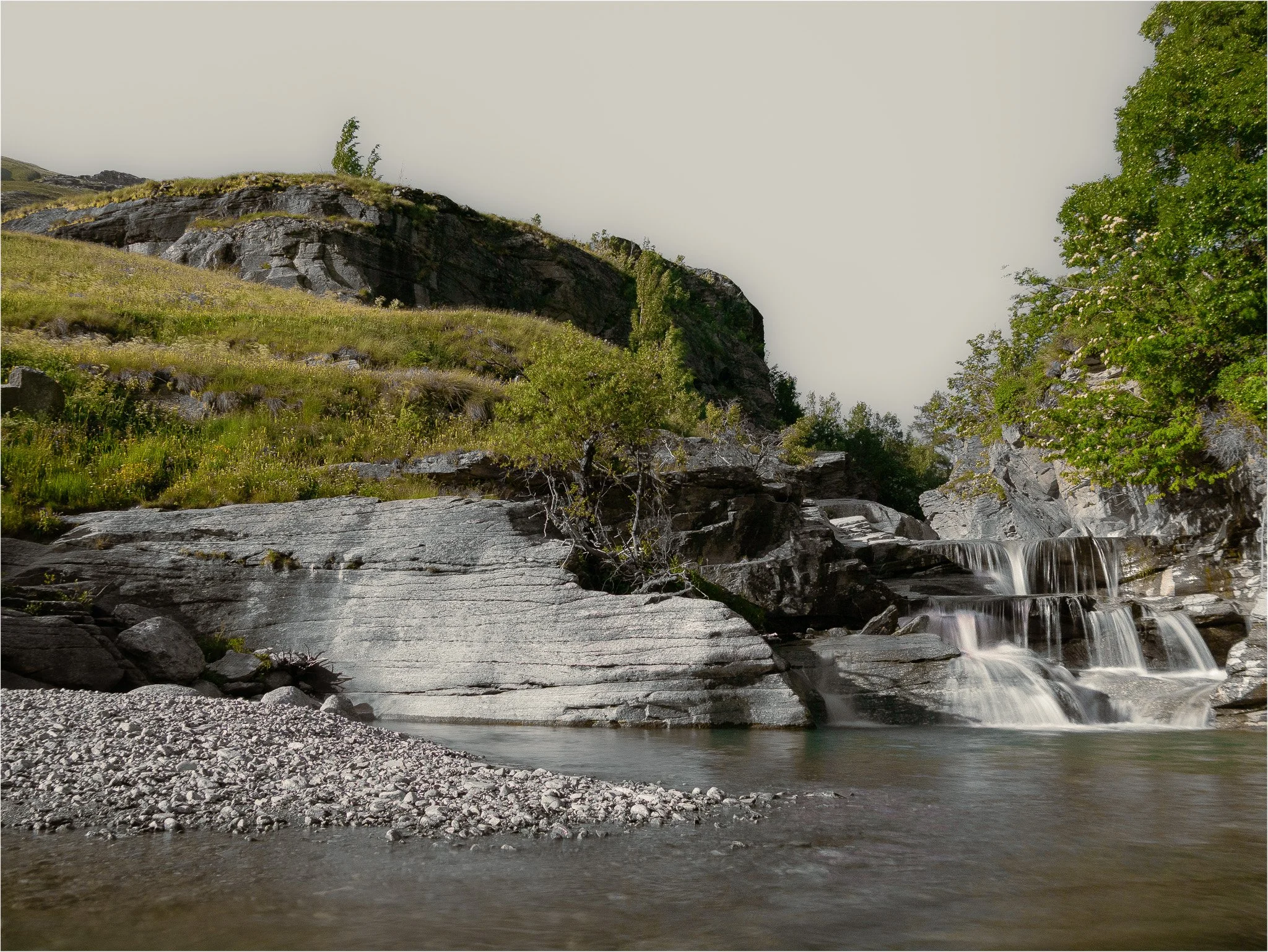 Une cascade coule sur des rochers au fond d'une vallée bordée d'arbres et de collines verdoyantes
