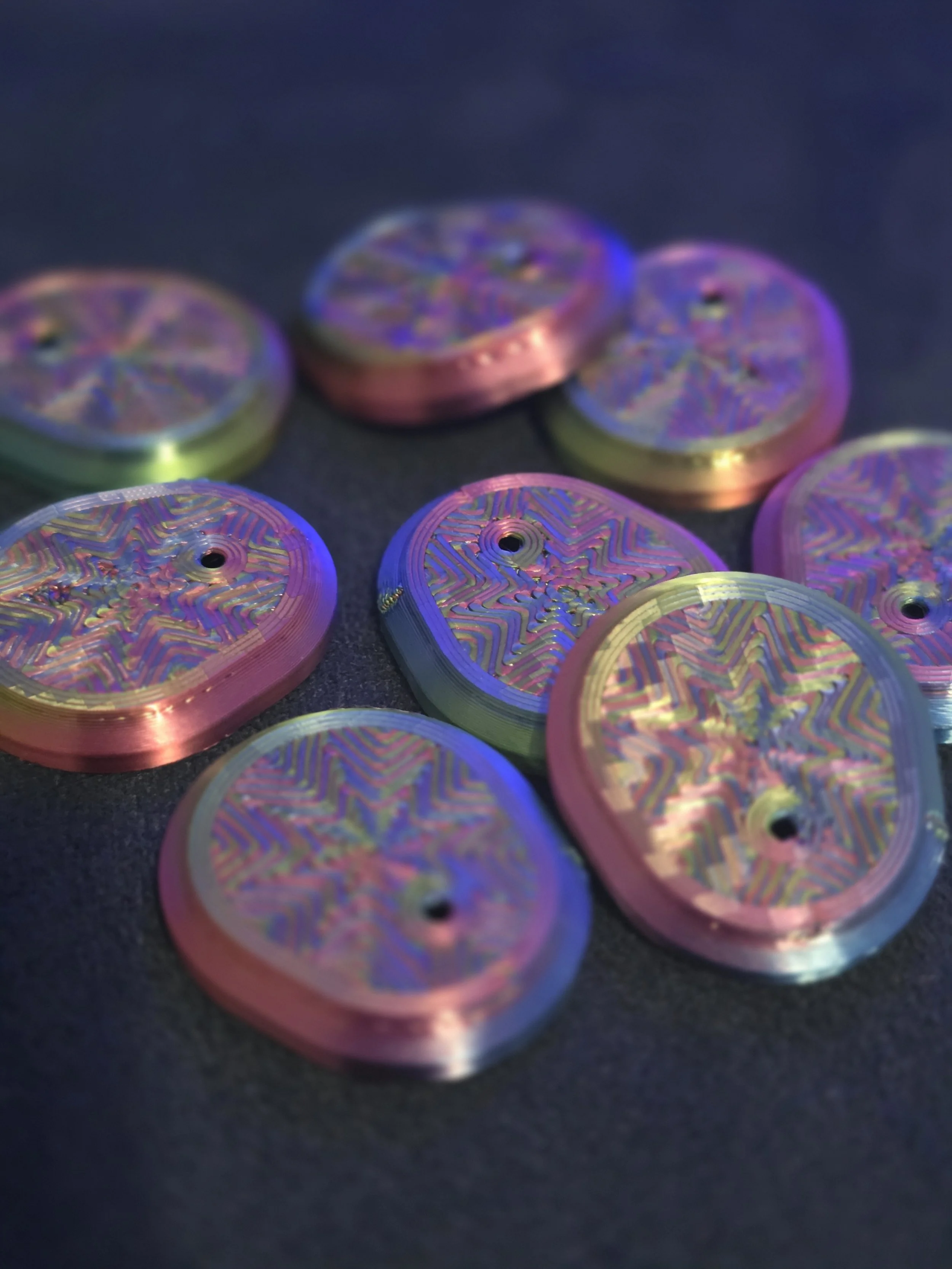 Colorful metallic coins with intricate rainbow patterns on a dark surface.
