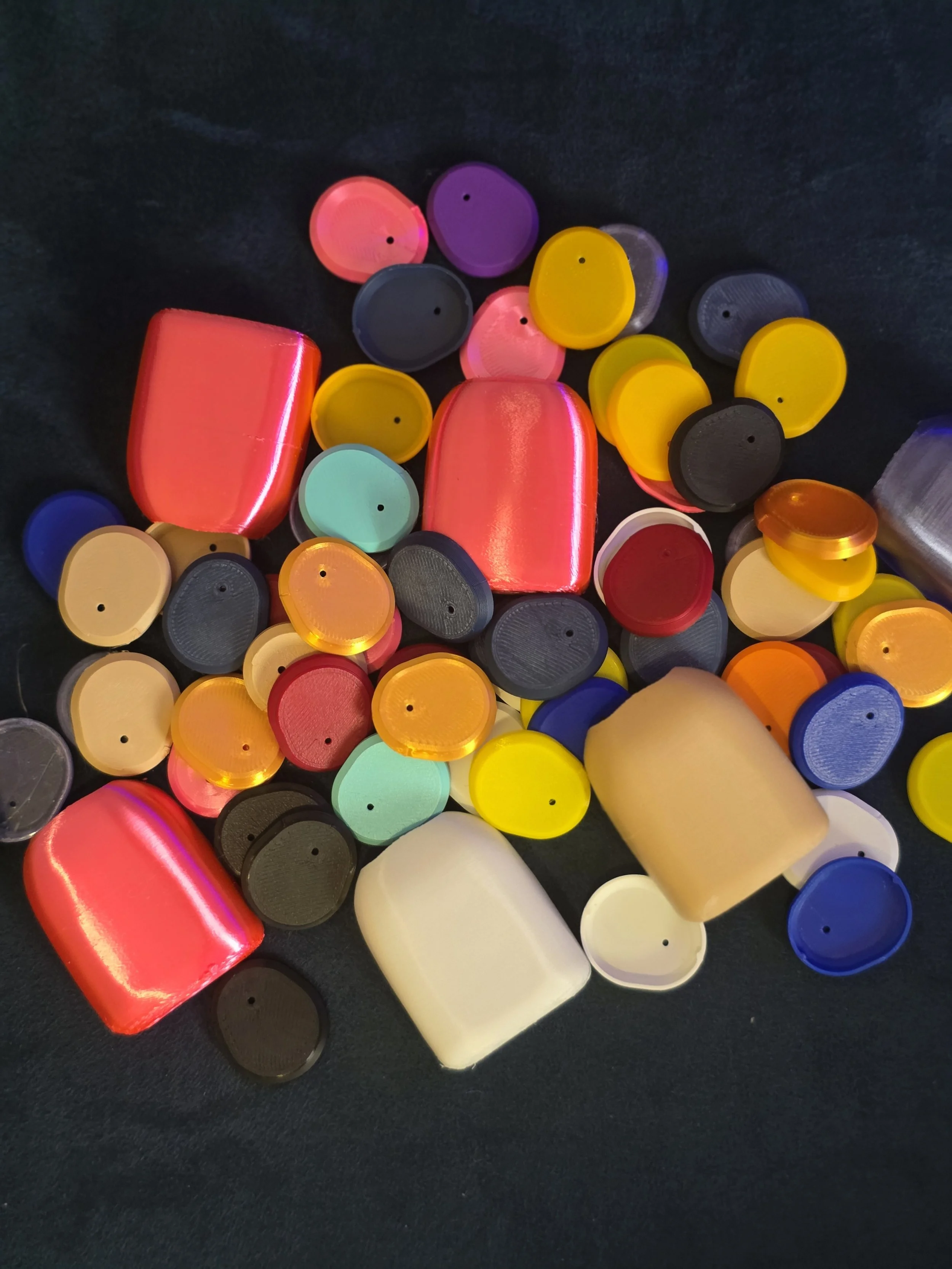 Colorful plastic bottle caps scattered on a dark surface, including red, purple, yellow, black, blue, white, and translucent caps.