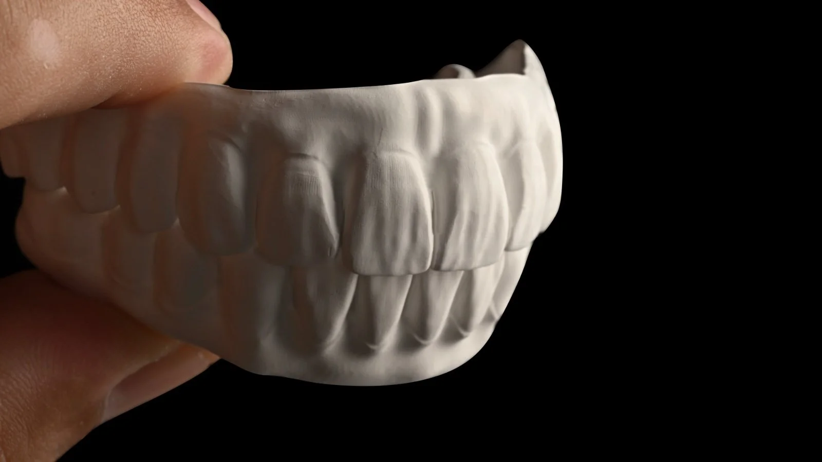 Close-up of a mold or sculpture depicting human teeth, held by a person's fingers against a black background.