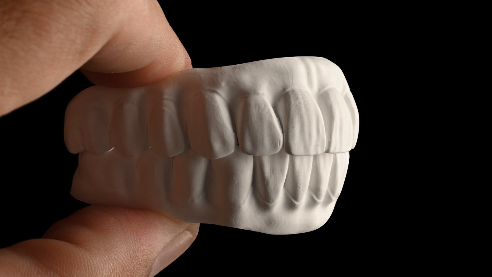 A close-up of a white dental mold showing teeth with a hand holding it, against a black background.