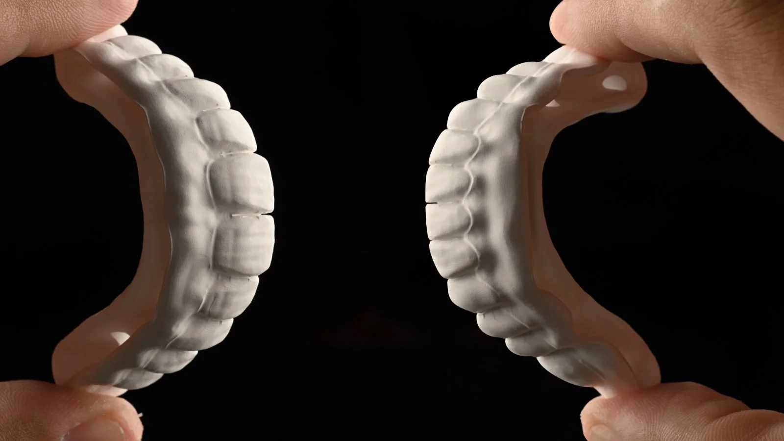 Human hands holding a dental model of teeth against a black background