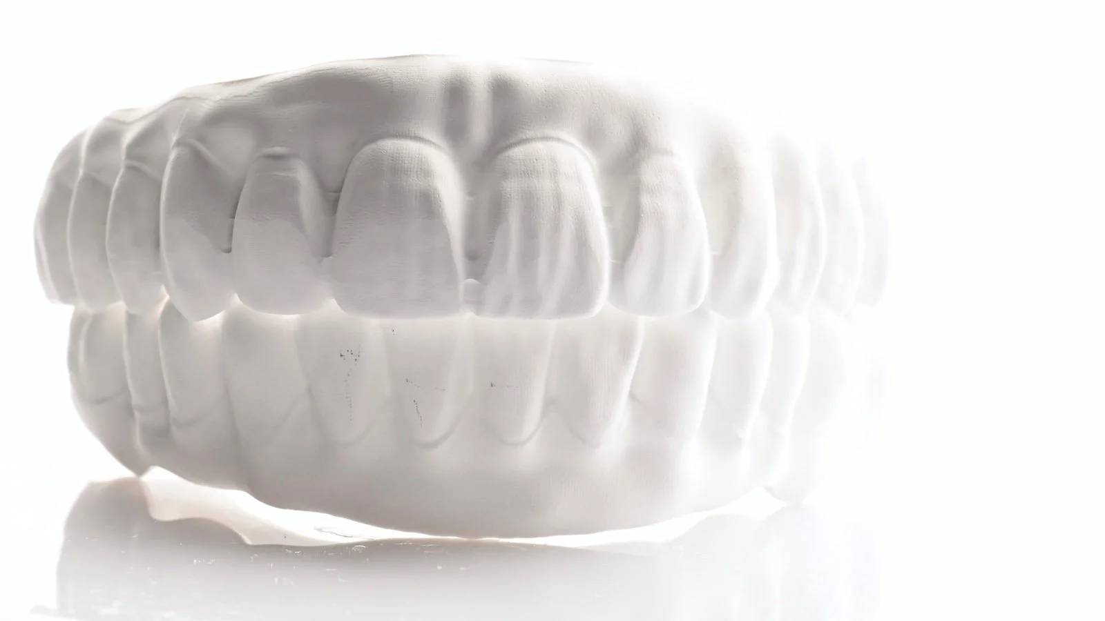 A white, abstract, sculptural piece resembling a human mouth with teeth, set against a white background.