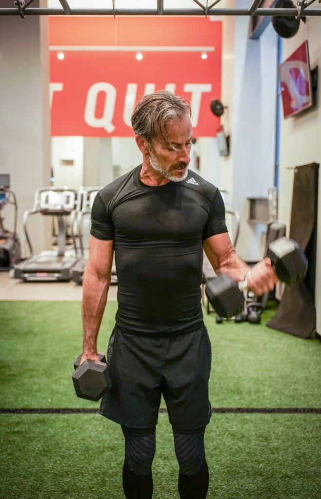 Garrett Swann (@thegarrettswann) silver fox fitness model sweating during dumbbell workout at NYSC Wall Street gym for Come Dry Leave Wet campaign wearing Adidas compression shirt, dont quit sign