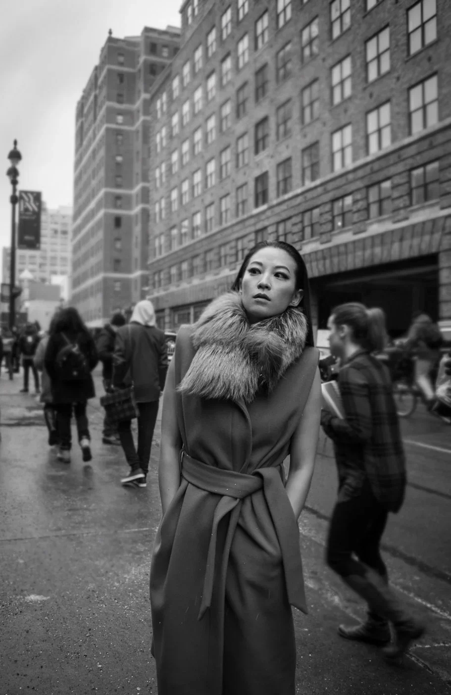 Black and white editorial street style portrait of actress and artist Arden Cho (@arden_cho) at New York Fashion Week (NYFW) in NYC. Shot by celebrity photographer Leonard 'Lenny Kats' Katsel, featuring Cho wearing a belted winter coat with a fur col