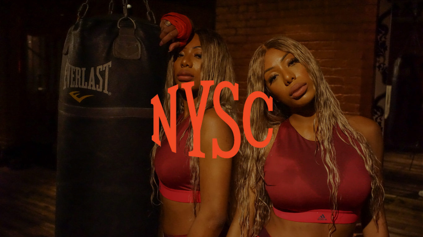 Clermont Twins Shannon and Shannade in red sportswear beside a heavy bag at a New York Sports Club boxing gym, campaign photography by Leonard Katsel | Lenny Kats