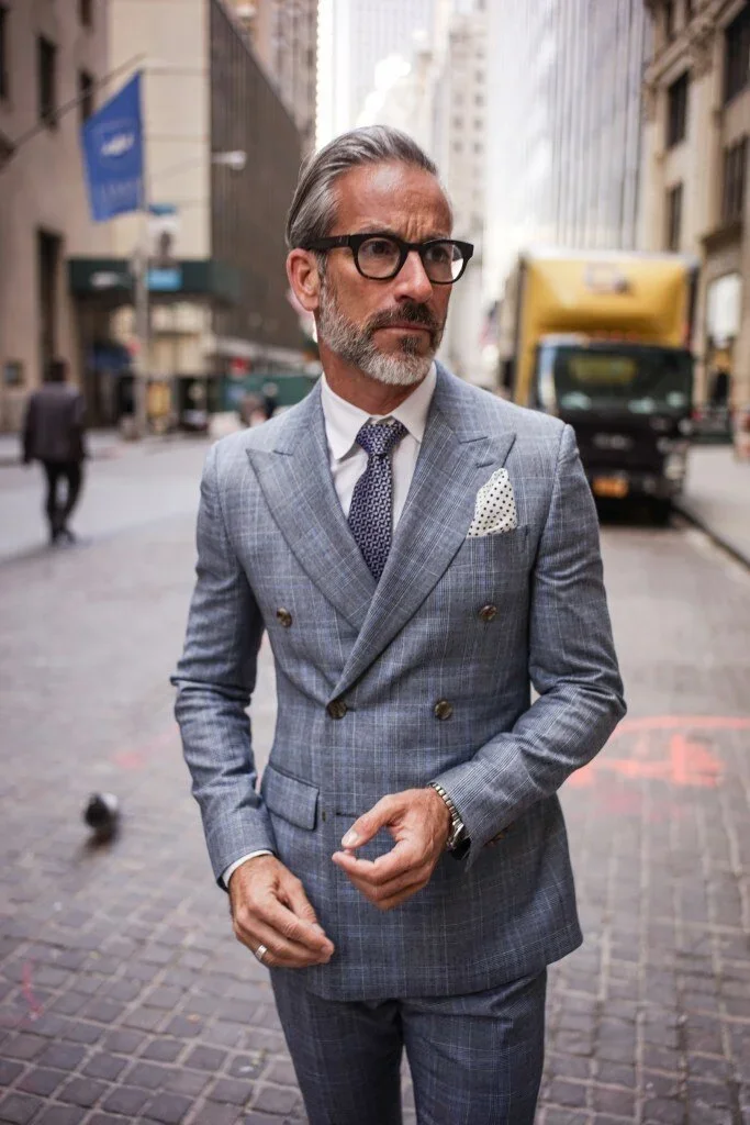 Garrett Swann (@thegarrettswann) silver fox male model on Wall Street NYC for NYSC Come Dry Leave Wet campaign wearing double breasted grey plaid suit with pocket square and glasses, street style portrait