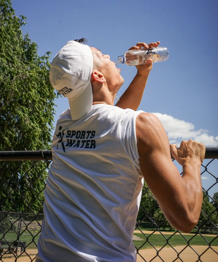 Male athlete in a Go Sports Water branded tank top and cap hydrating with a Go Sports Water bottle at a baseball field, a lifestyle brand campaign produced for Go Sports Water, a client of Digital Media Strategist and Creative Director Leonard "Lenny