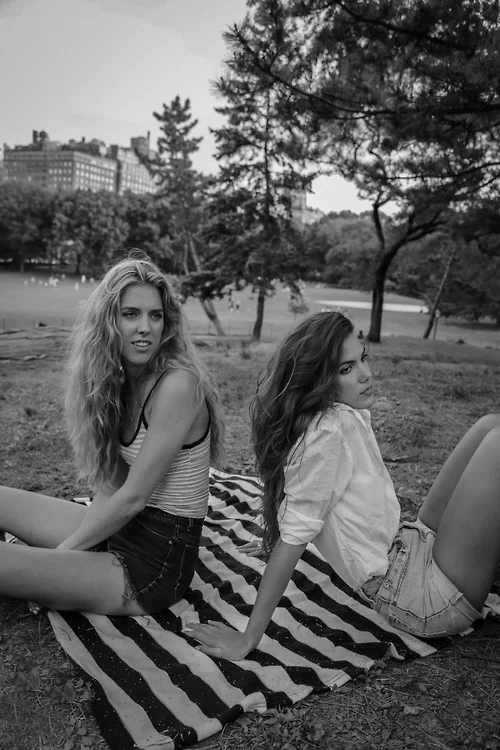 Twin female models sitting on a striped picnic blanket in Central Park, NYC; black and white lifestyle portrait photography by Leonard Lenny Kats Katsel