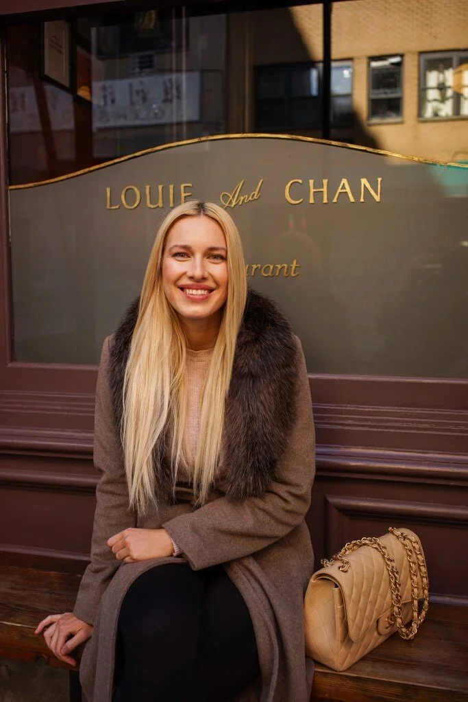 Doroshina (@doroshina) blonde model sitting outside Louie and Chan restaurant NYC wearing fur collar coat with Chanel quilted gold chain bag, street style portrait photography