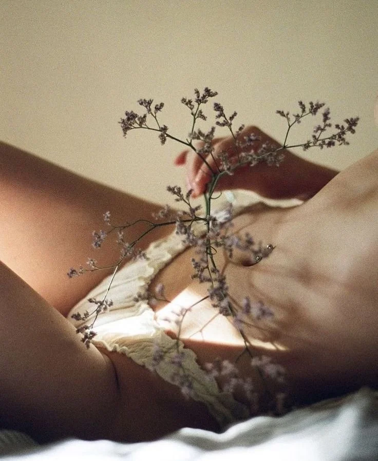 Close-up of a person lying down with a dried flower branch in the foreground, only part of their torso and hand visible.
