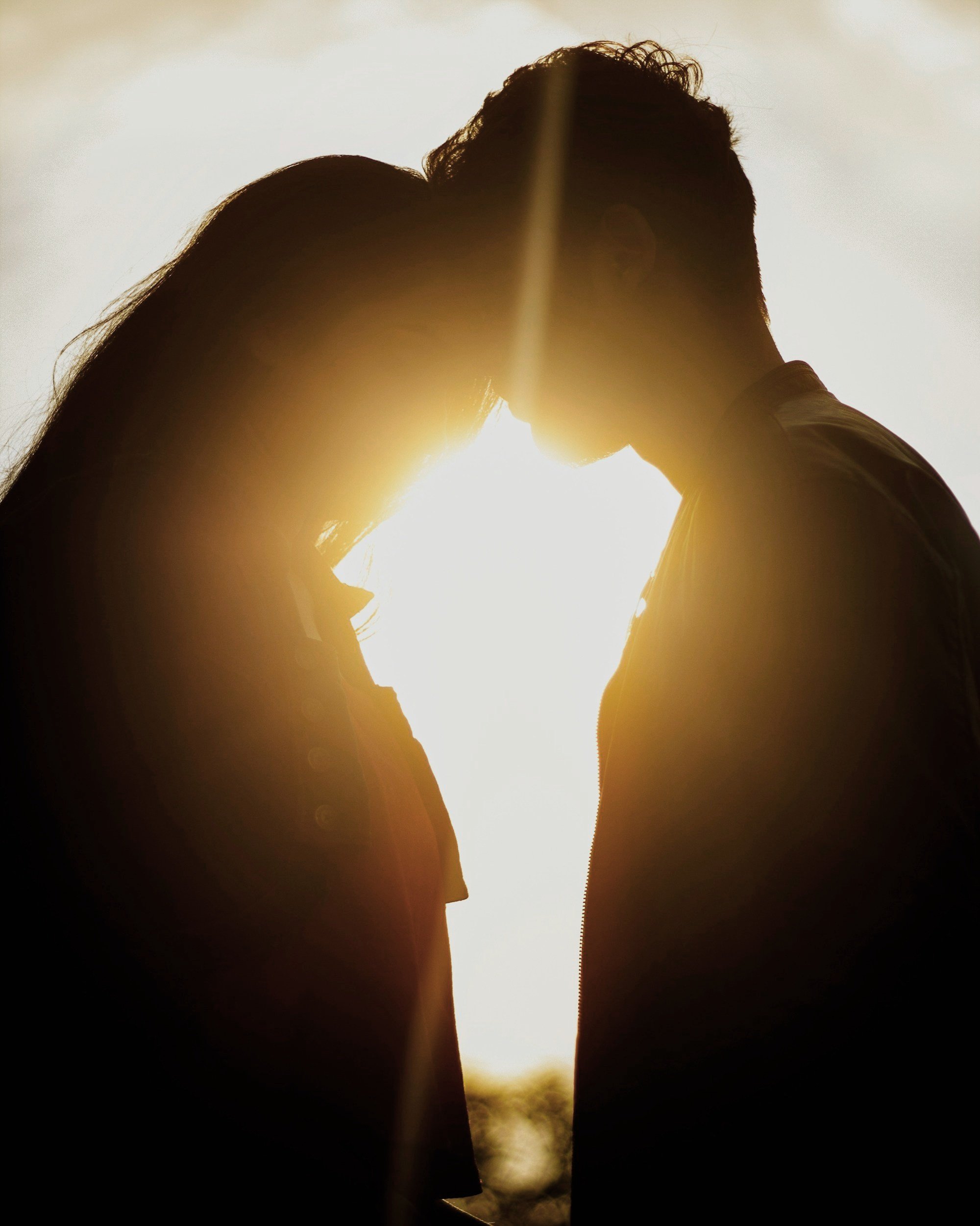 Silhouette of a couple facing each other at sunset, with their foreheads touching and eyes closed, creating a romantic ambiance.