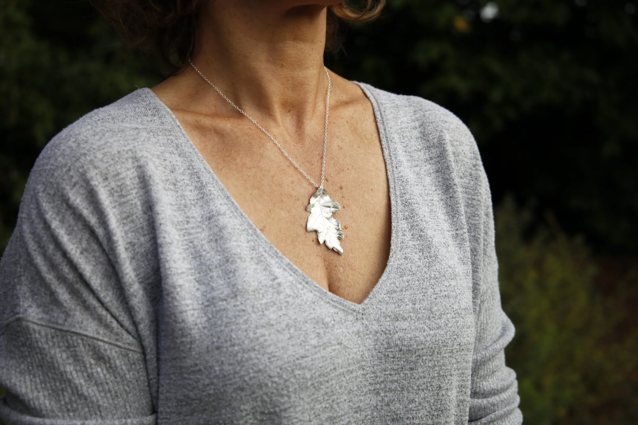 A woman wearing a gray sweatshirt and a silver leaf-shaped necklace.
