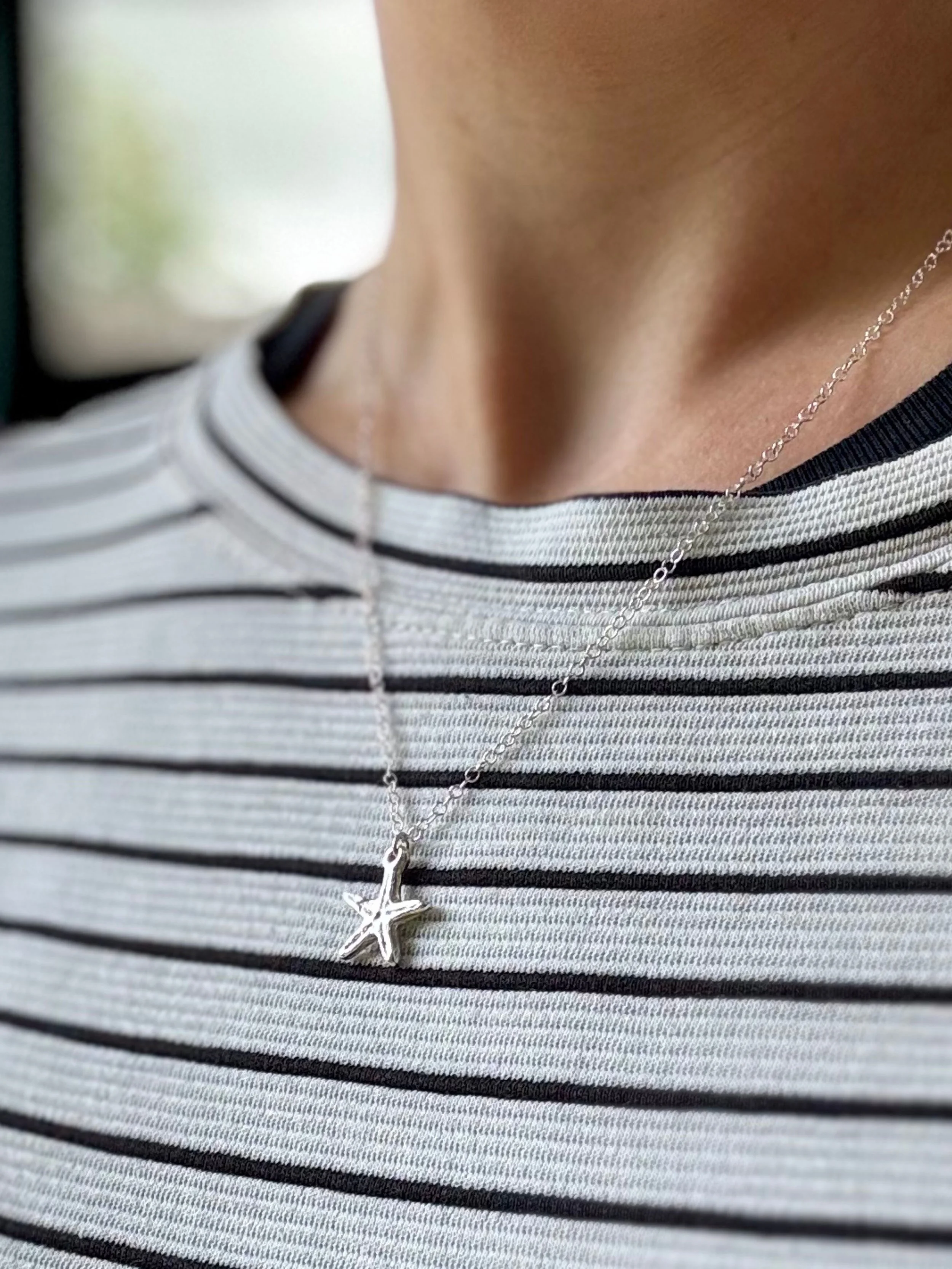 Close-up of a person wearing a silver star-shaped necklace and a striped shirt with black, white, and gray horizontal lines.