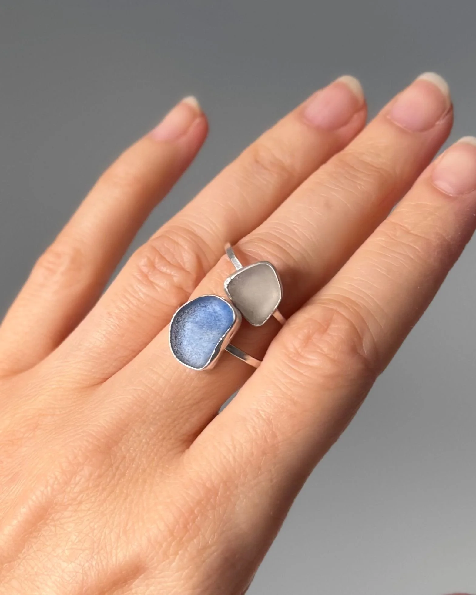 Close-up of a hand wearing two sea glass rings, against a plain background.