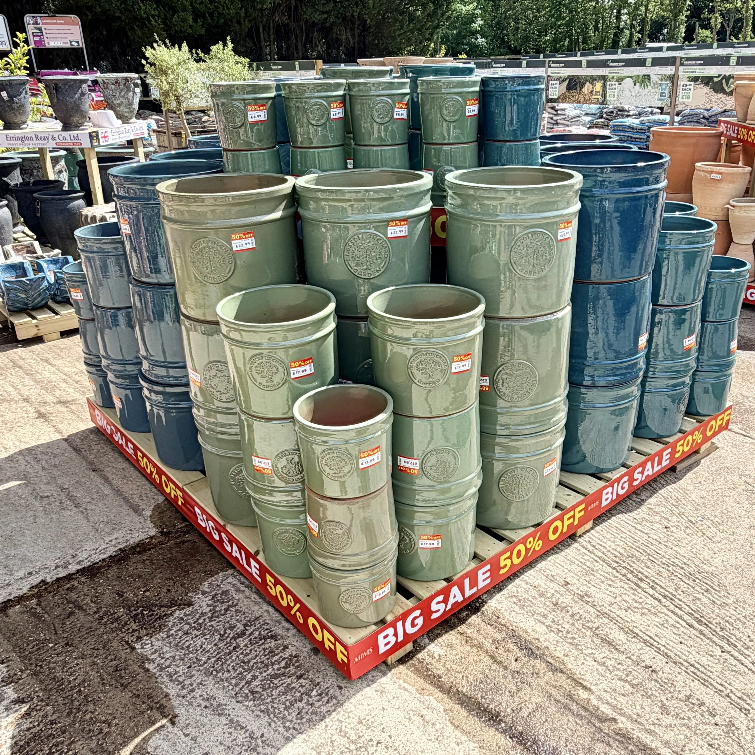 Stacked green and blue ceramic plant pots on display at an outdoor garden center, with sale signs indicating 50% off.