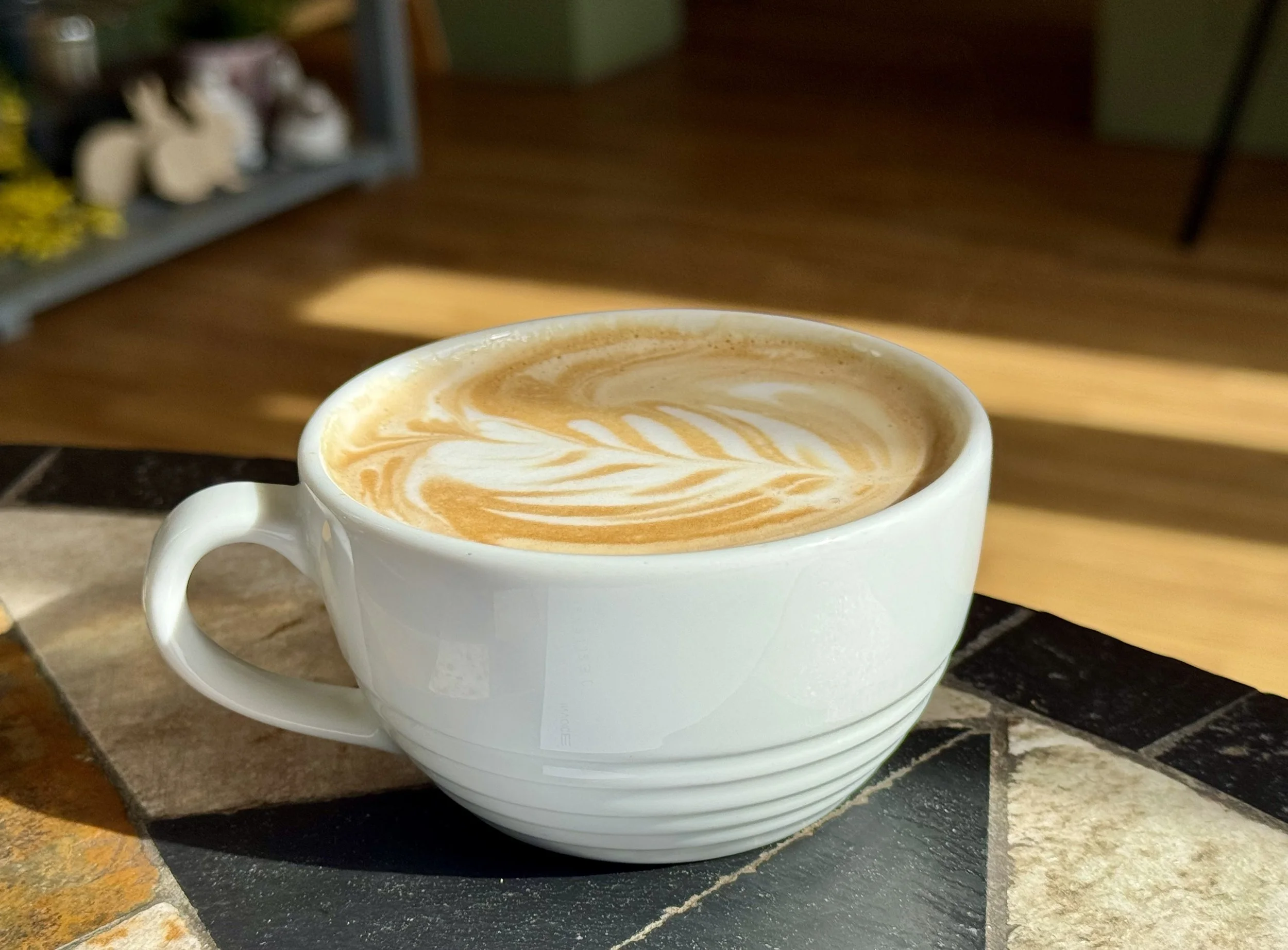 A white ceramic cup of coffee with latte art on top, placed on a saucer and stacked with other cups on a counter.