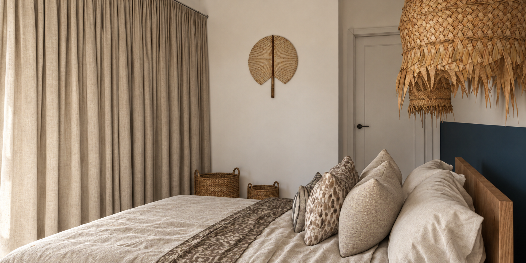 Chambre avec un lit décoré de coussins et de draps beige, rideaux lourds en tissu beige, décoration murale en forme de feuille en rotin, luminaires en bambou suspendus, panier en osier à côté du lit.