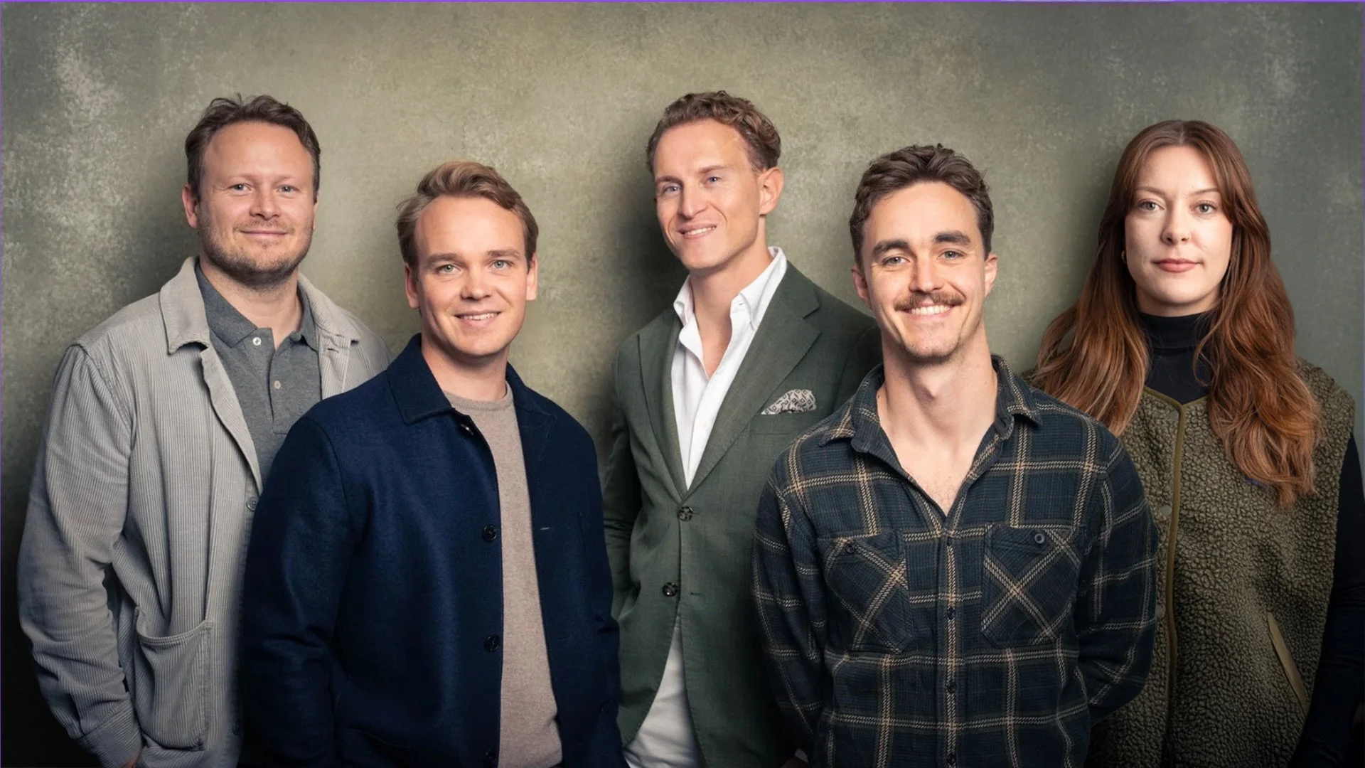 Group of six adults – Explainer employees – standing against a plain background, smiling and looking at the camera.