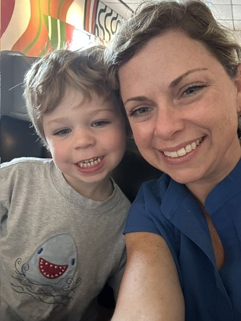 A woman and young boy taking a selfie together in a brightly decorated indoor setting, both smiling at the camera. Working on speech therapy goals.