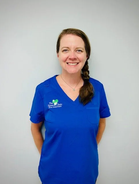 Woman in blue scrubs smiling against a plain light gray background.  A therapist with The Speech Clinic of the Coastal Empire in Savannah GA.