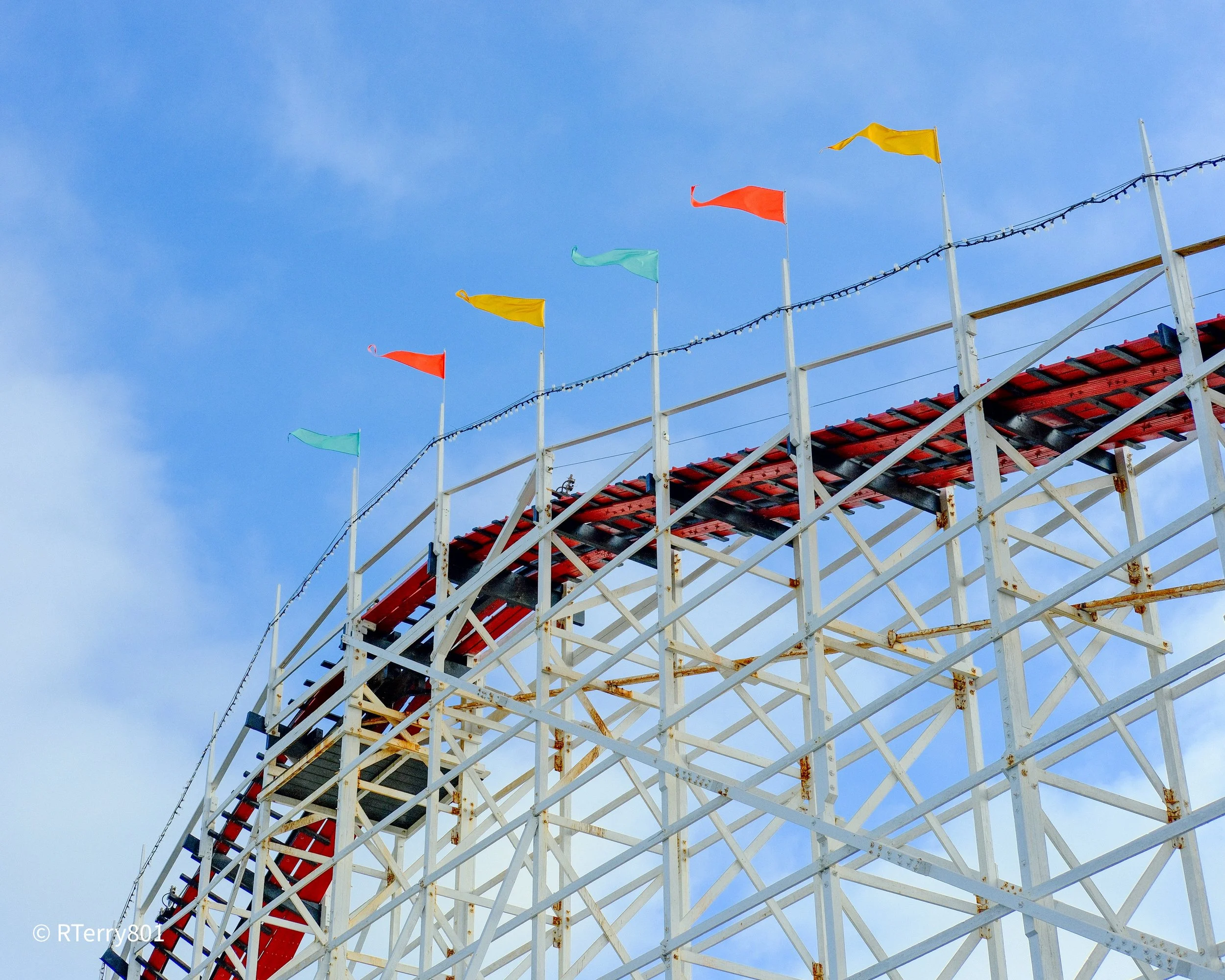 Colorful flags on poles and a wooden structure against a blue sky.