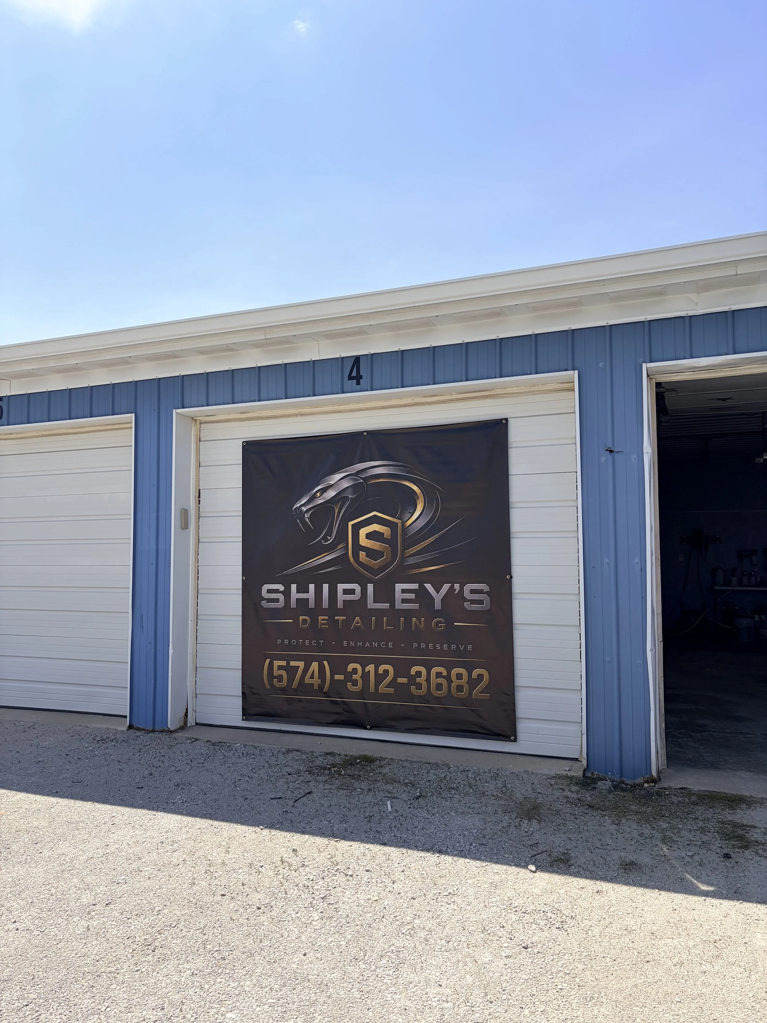 Front of building with a large banner for Shipley's Detailing, displaying a logo of a stylized animal head and text including the phone number (574) 312-3682.