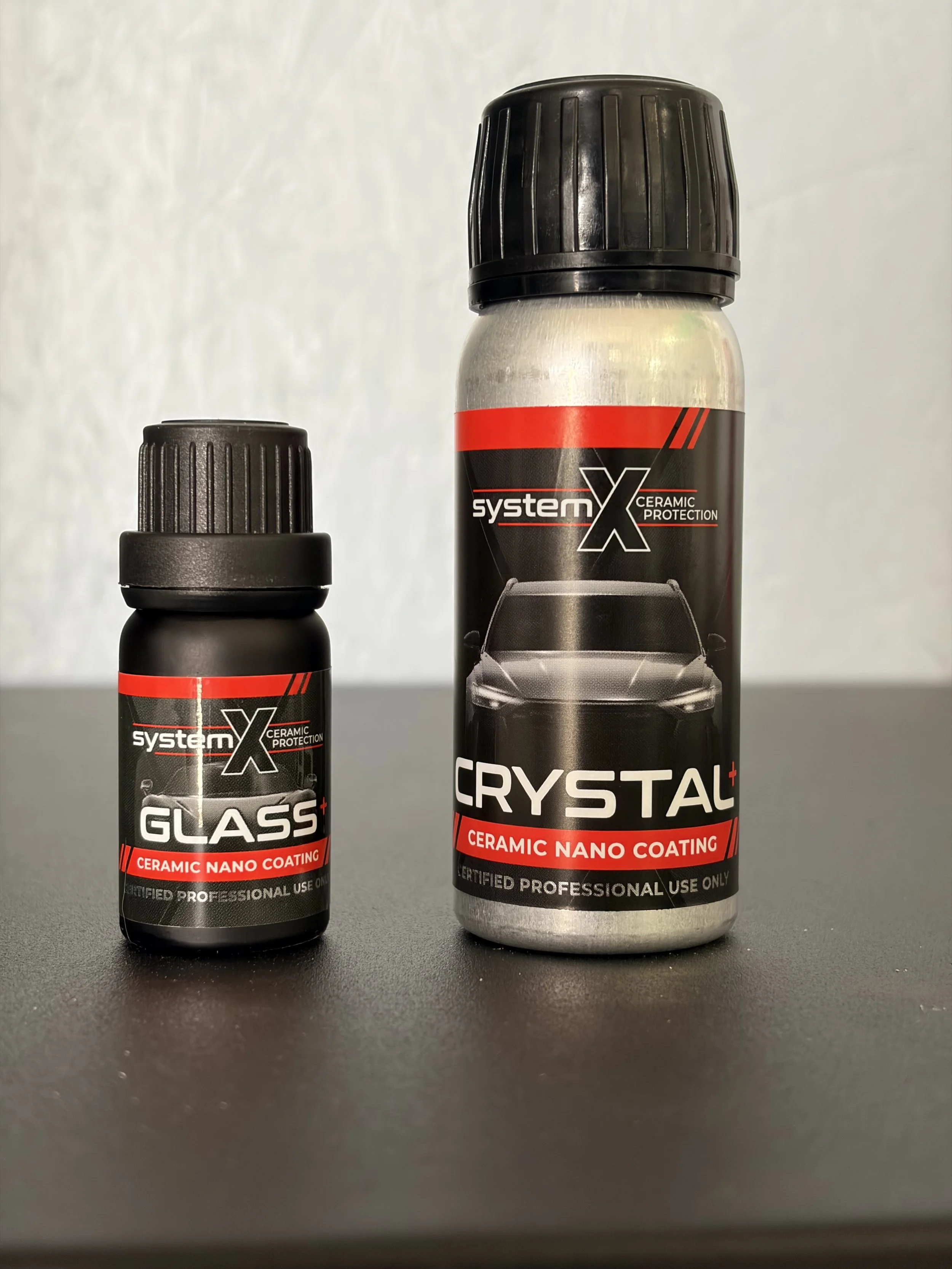 Two cans of ceramic nano coating products, one labeled 'Glass+' and the other 'Crystal+', on a dark surface against a plain light background.