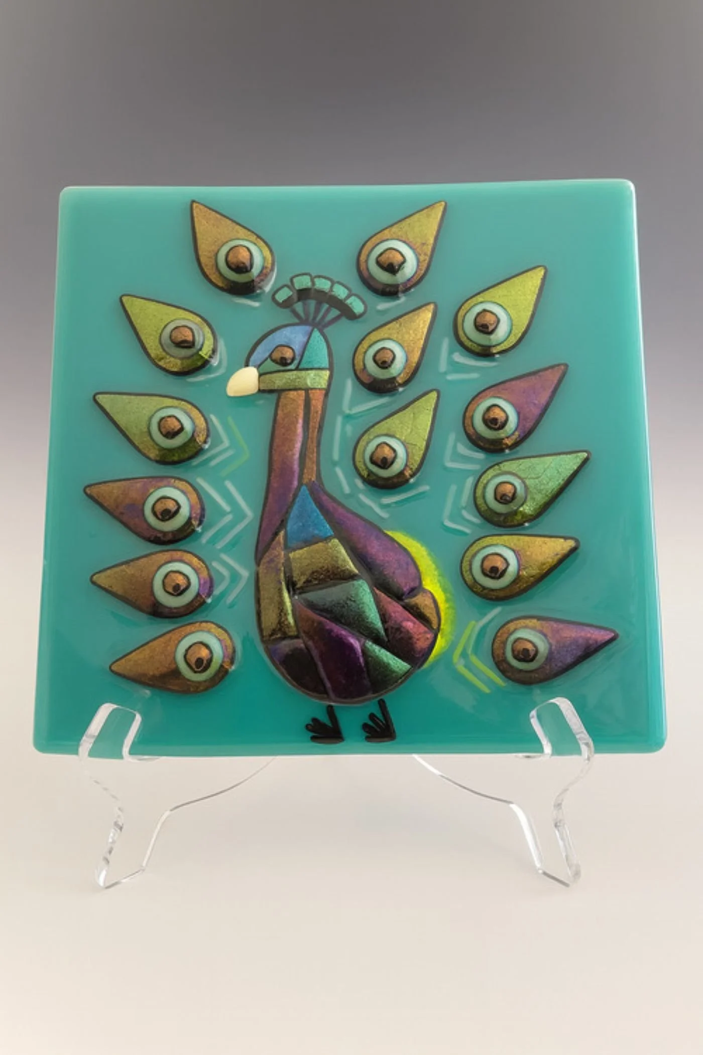 Fused glass tile featuring an iridescent peacock on a turquoise background. 8 x 8 inch. $116.