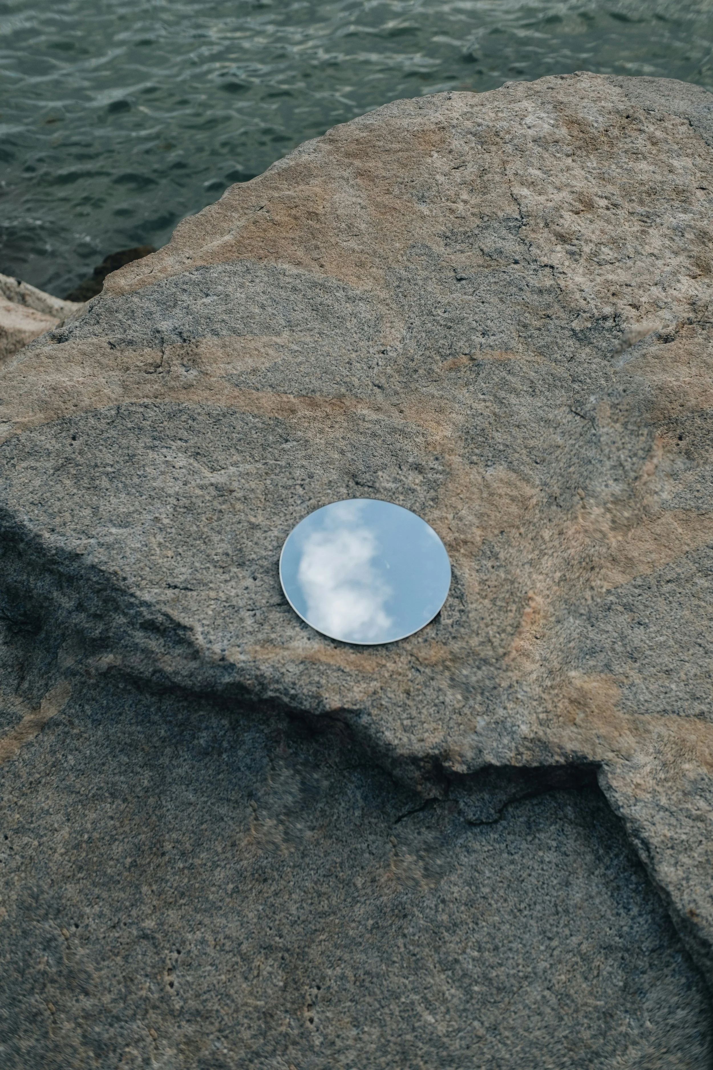 circular mirror on a rock by the sea, reflecting the clouds
