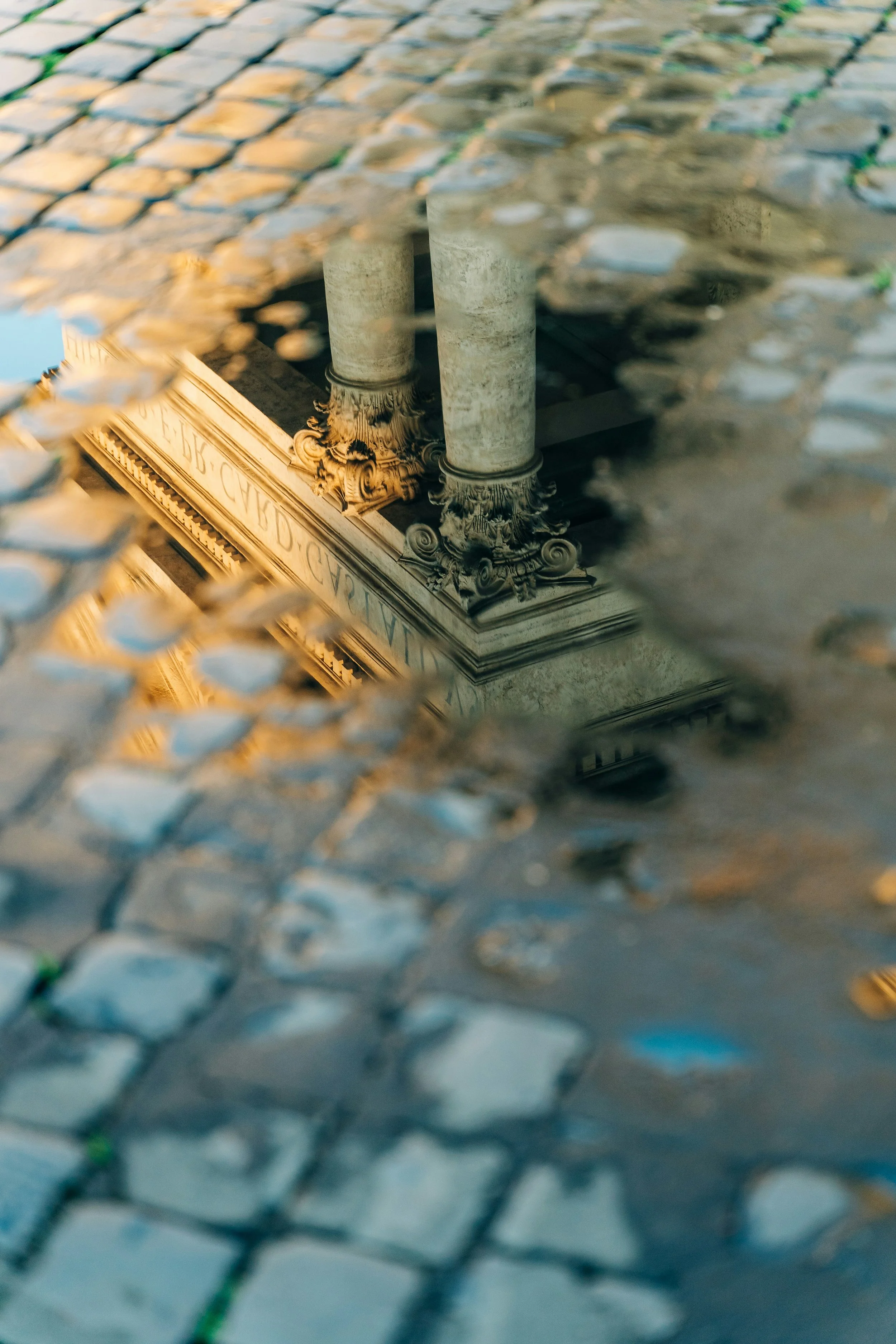colour photo of a reflection of intricate pillars of a grand building, golden light and cobbled stone
