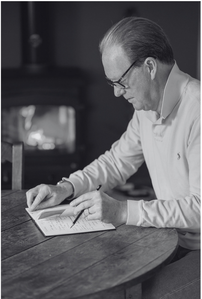 black and white photo of coach and writer Myles Downey at a desk writing with an open fire in the background