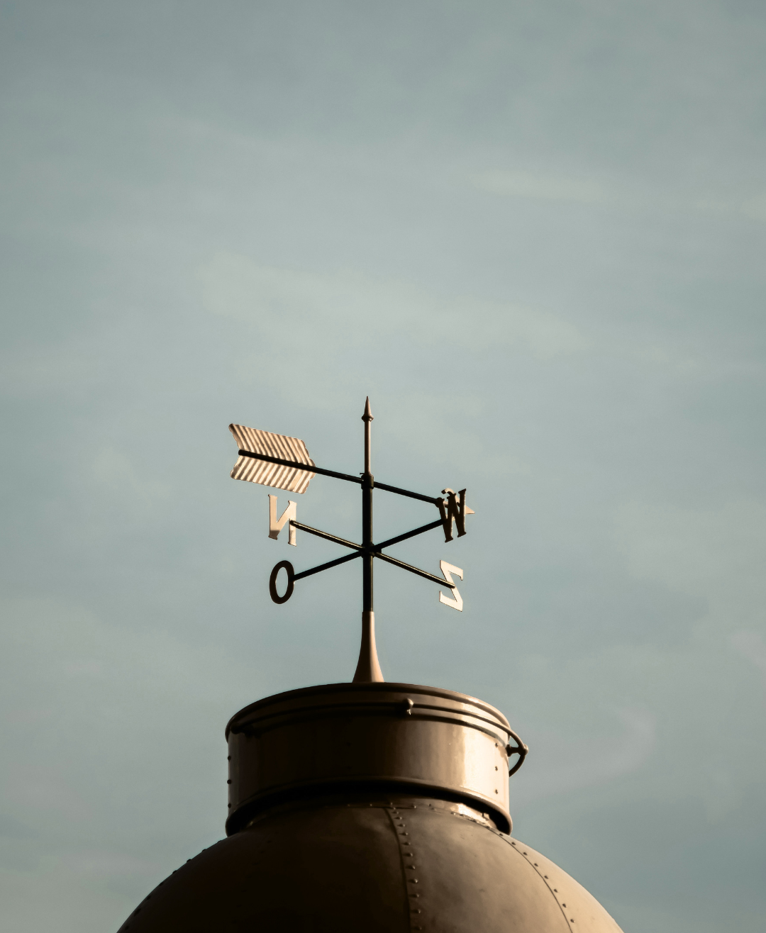 photo of a golden weather vane with sky behind