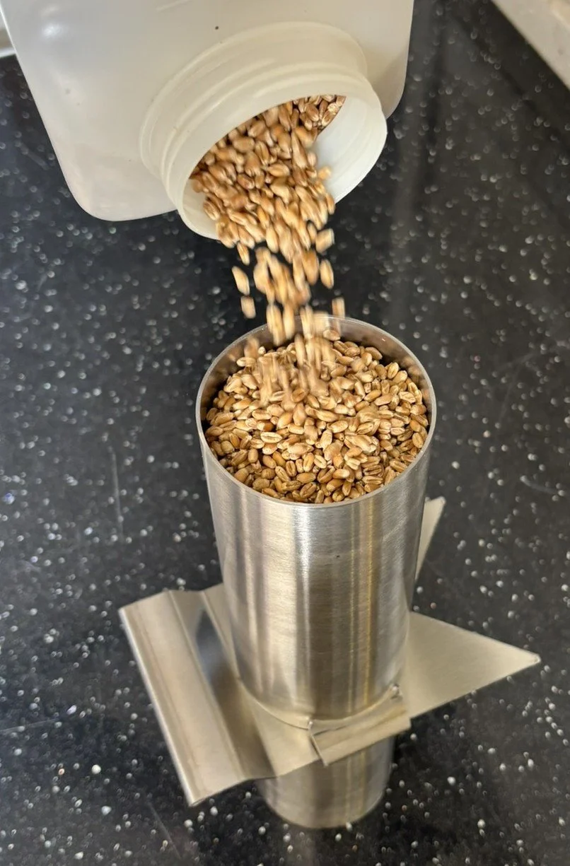 Grains being dispensed into a metal container from a white plastic container above, on a speckled black surface.