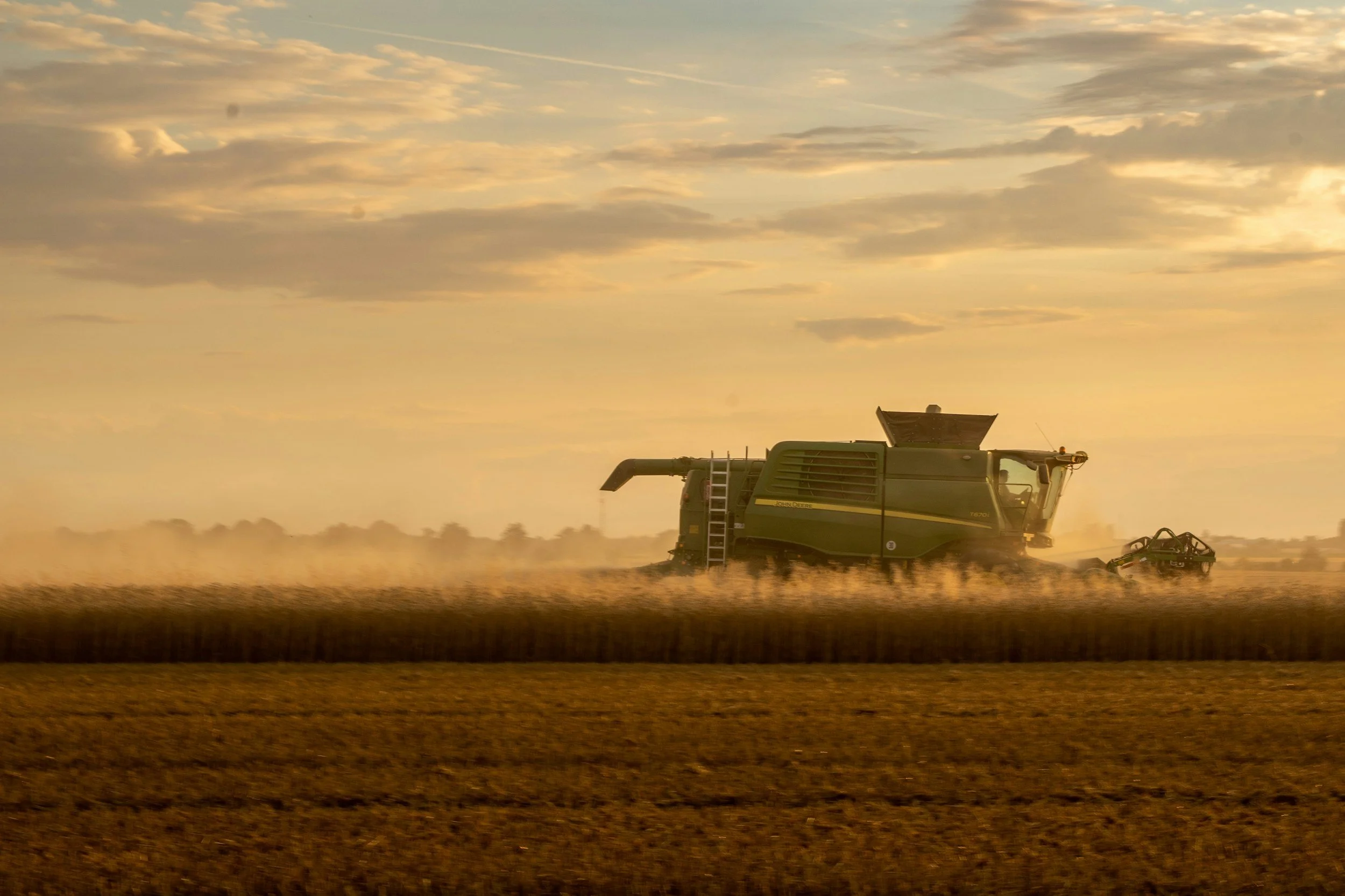 A combine harvester working in a field during sunset, with clouds and a yellow sky in the background.