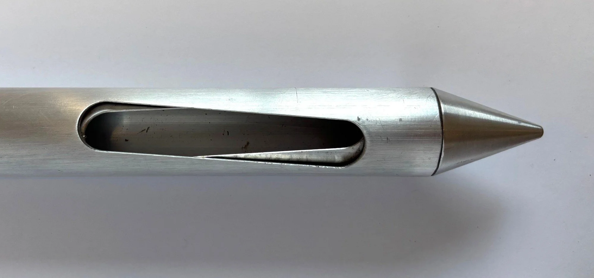 Close-up of a metal pipe with an oval-shaped opening and a pointed tip, placed on a white surface.