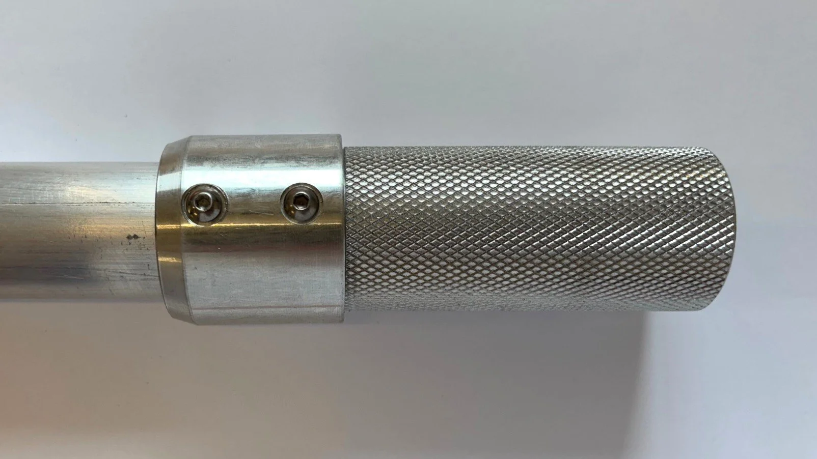 Close-up of a metallic cylindrical tool with a textured grip surface and screws visible on a plain background.