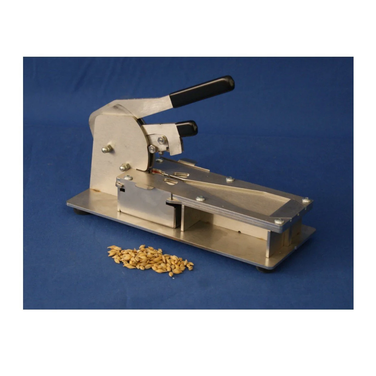 A metallic pumpkin seed sheller with black handles, placed on a blue background, with a small pile of pumpkin seeds nearby.