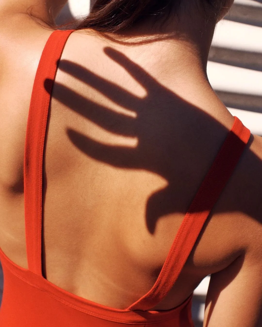 A person's shoulder and upper chest area wearing an orange tank top, with a shadow of a hand cast on the skin.