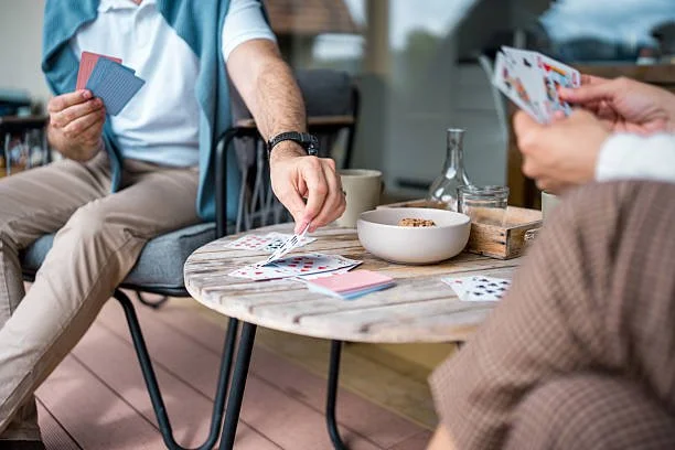 Two people playing cards at a round wooden table in a casual indoor setting.