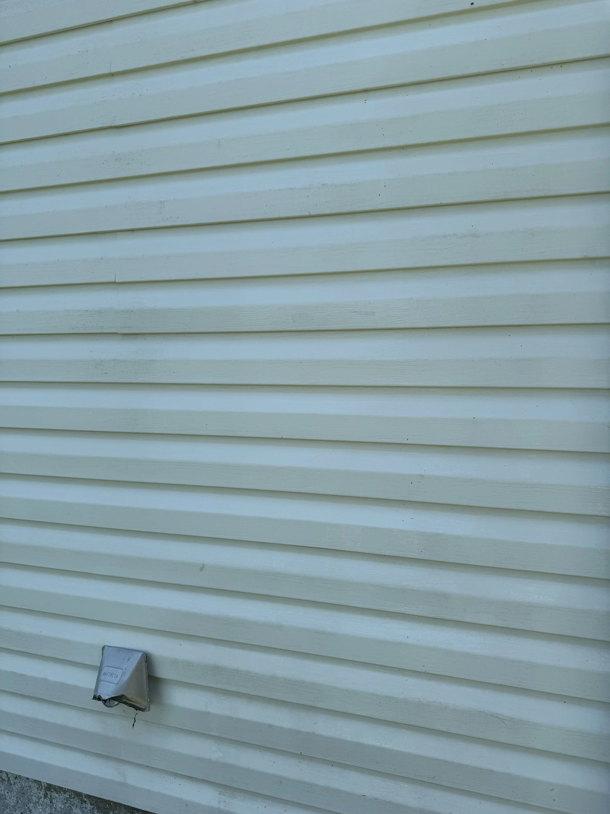 A beige house exterior with horizontal vinyl siding and a small metal electrical box mounted on the wall near the bottom left corner.