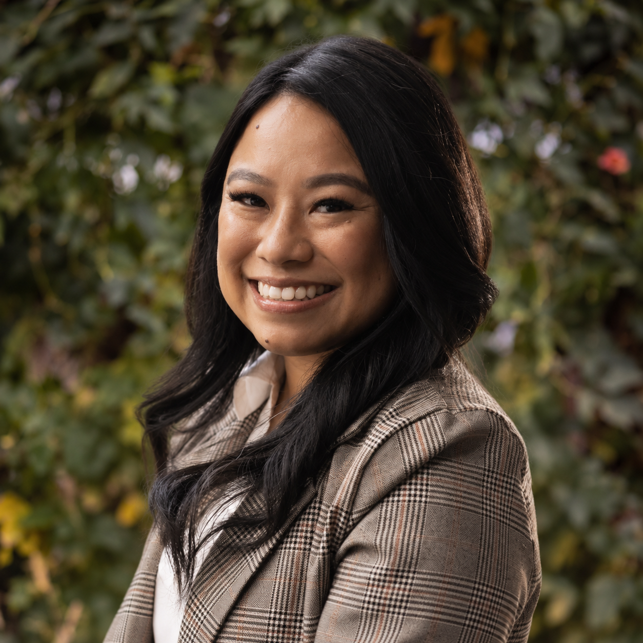 Portrait of a woman with medium length dark hair, smiling, wearing a plaid suit.