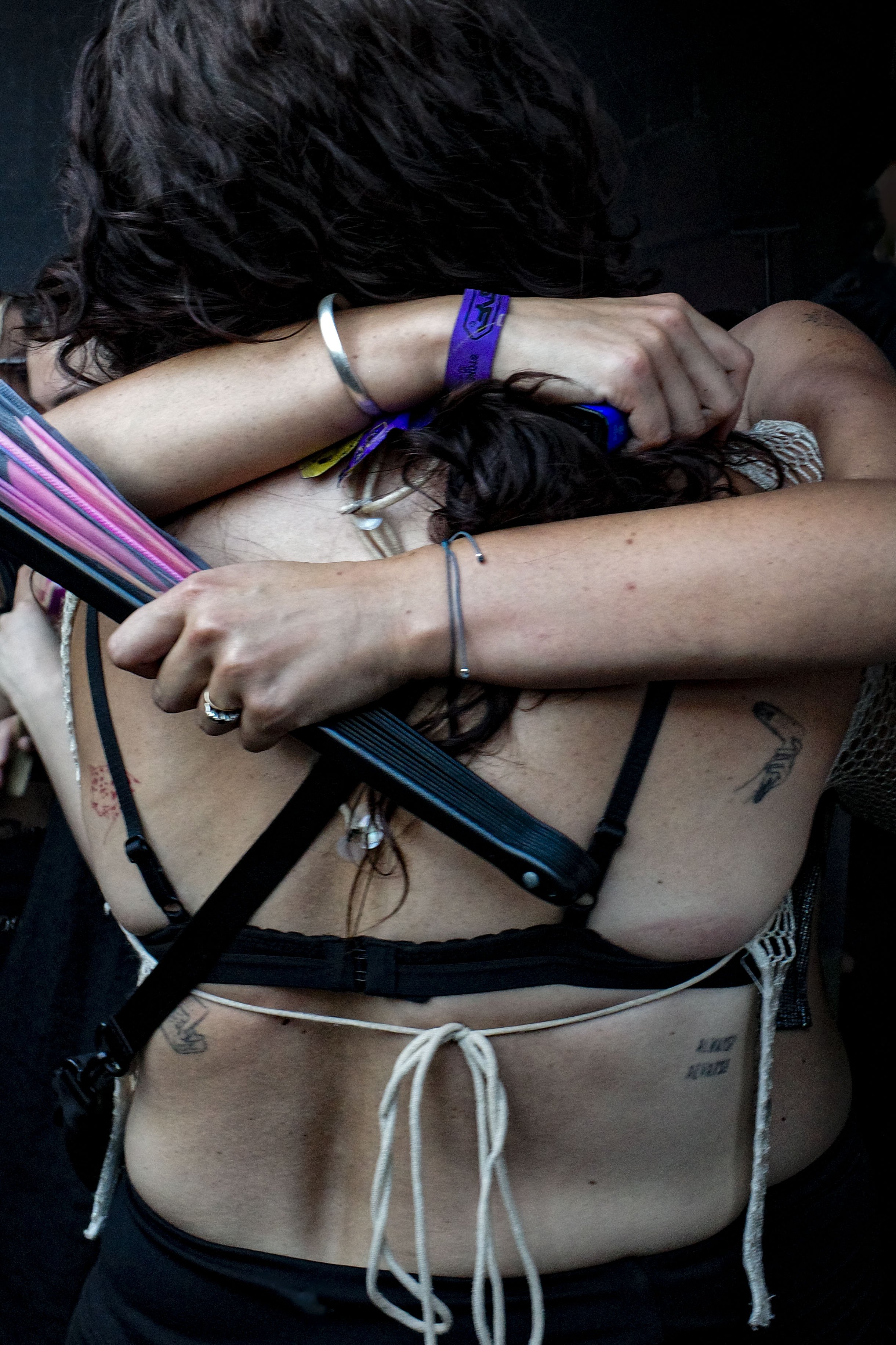 Close-up of a woman lying down, with her head resting on her arm and her face partially obscured, wearing a bracelet and multiple necklaces, with tattoos visible on her shoulder and side at Stone Techno Festival..