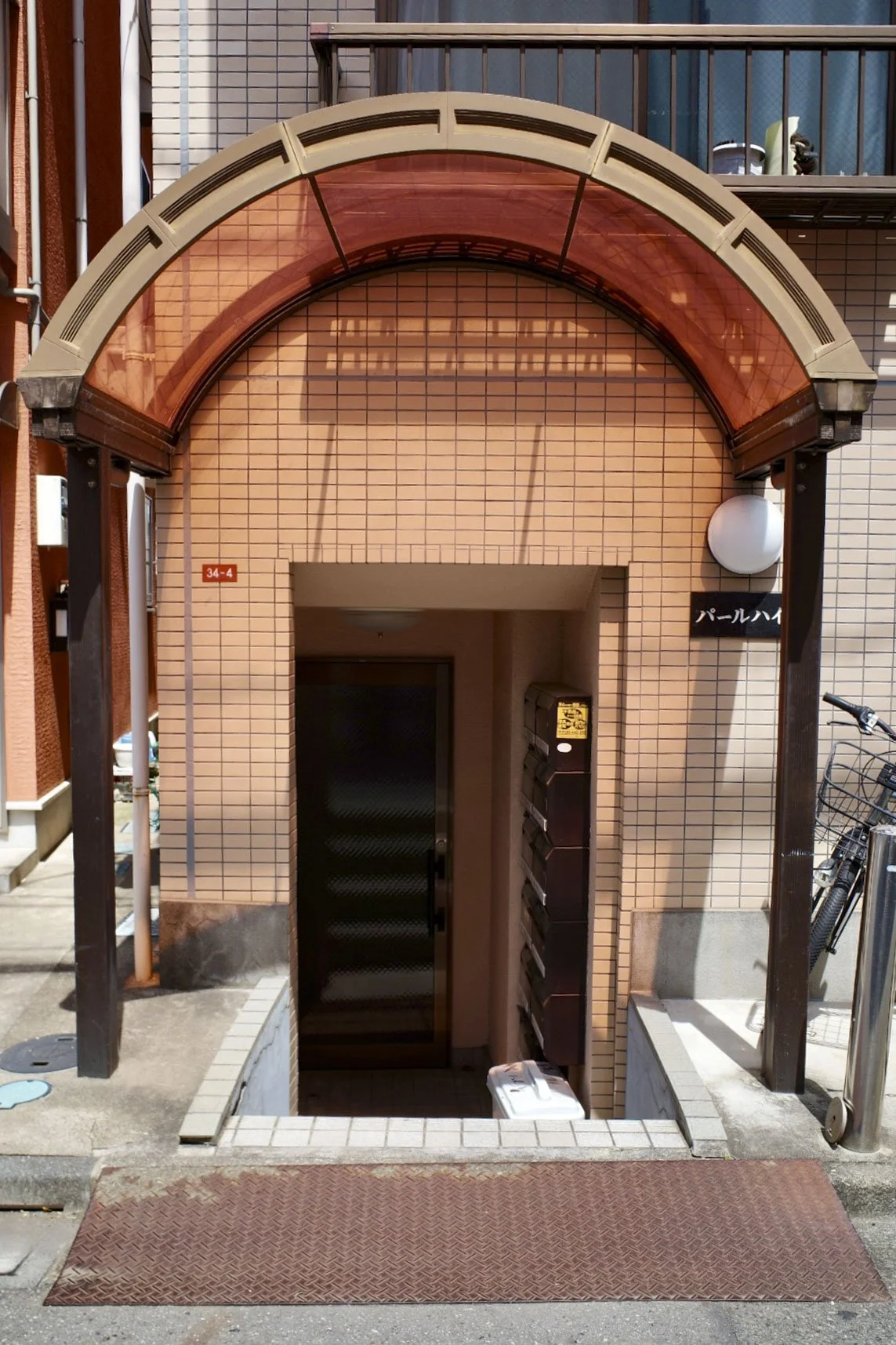 Entrance to a building with a tiled facade, an archway with a glass cover, mailboxes, a door leading underground, a bicycle, and Japanese signage in Tokyo, Japan.