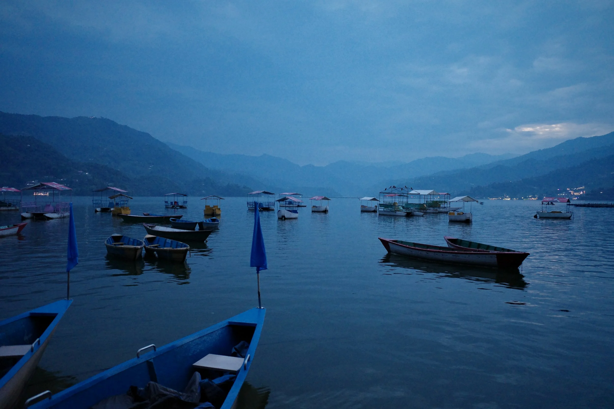 Several small boats floating on a calm lake with mountains in the background during dusk or dawn.