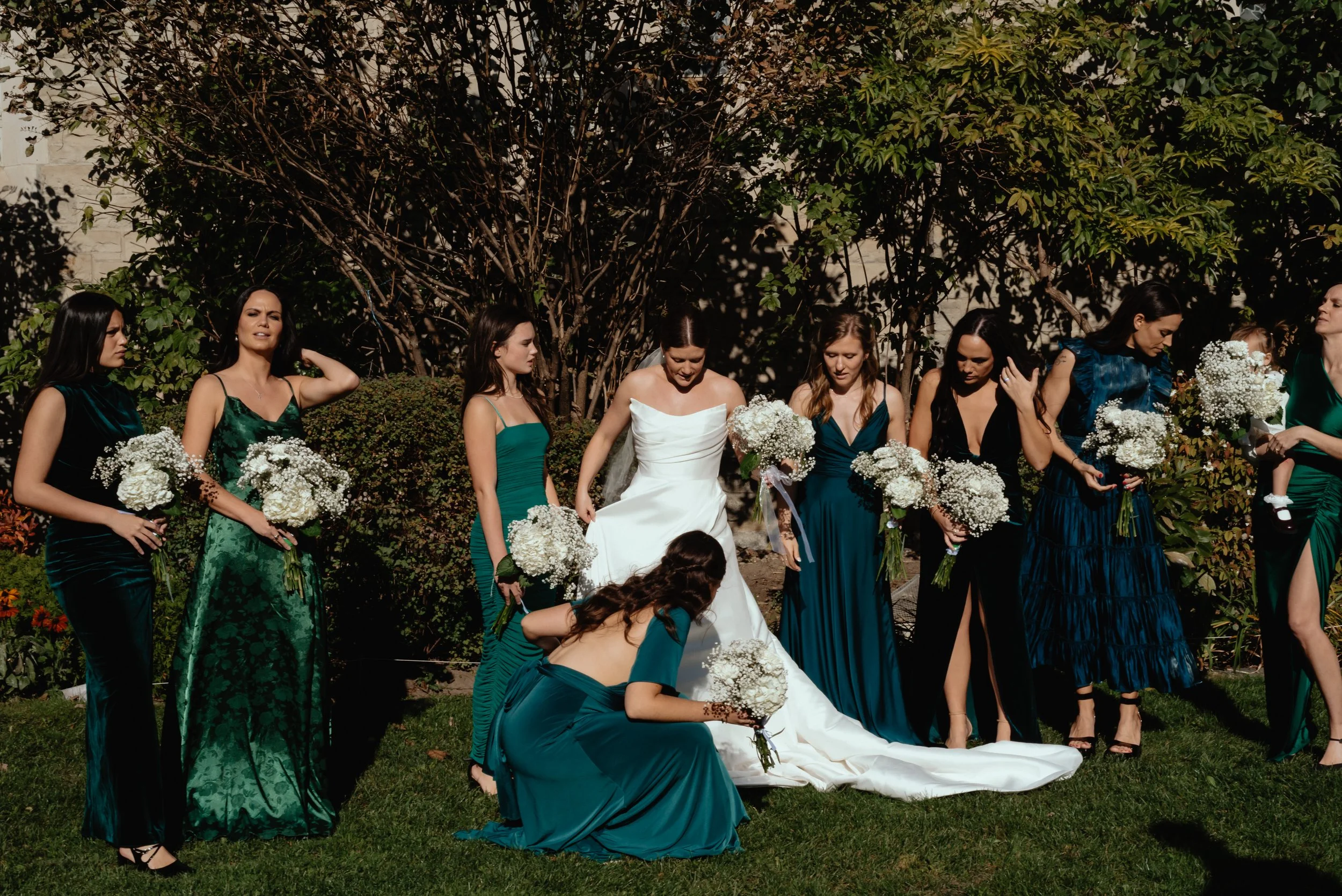 Candid behind-the-scenes moment of a bride and her bridal party adjusting their dresses, hair and bouquets before a formal wedding portrait.