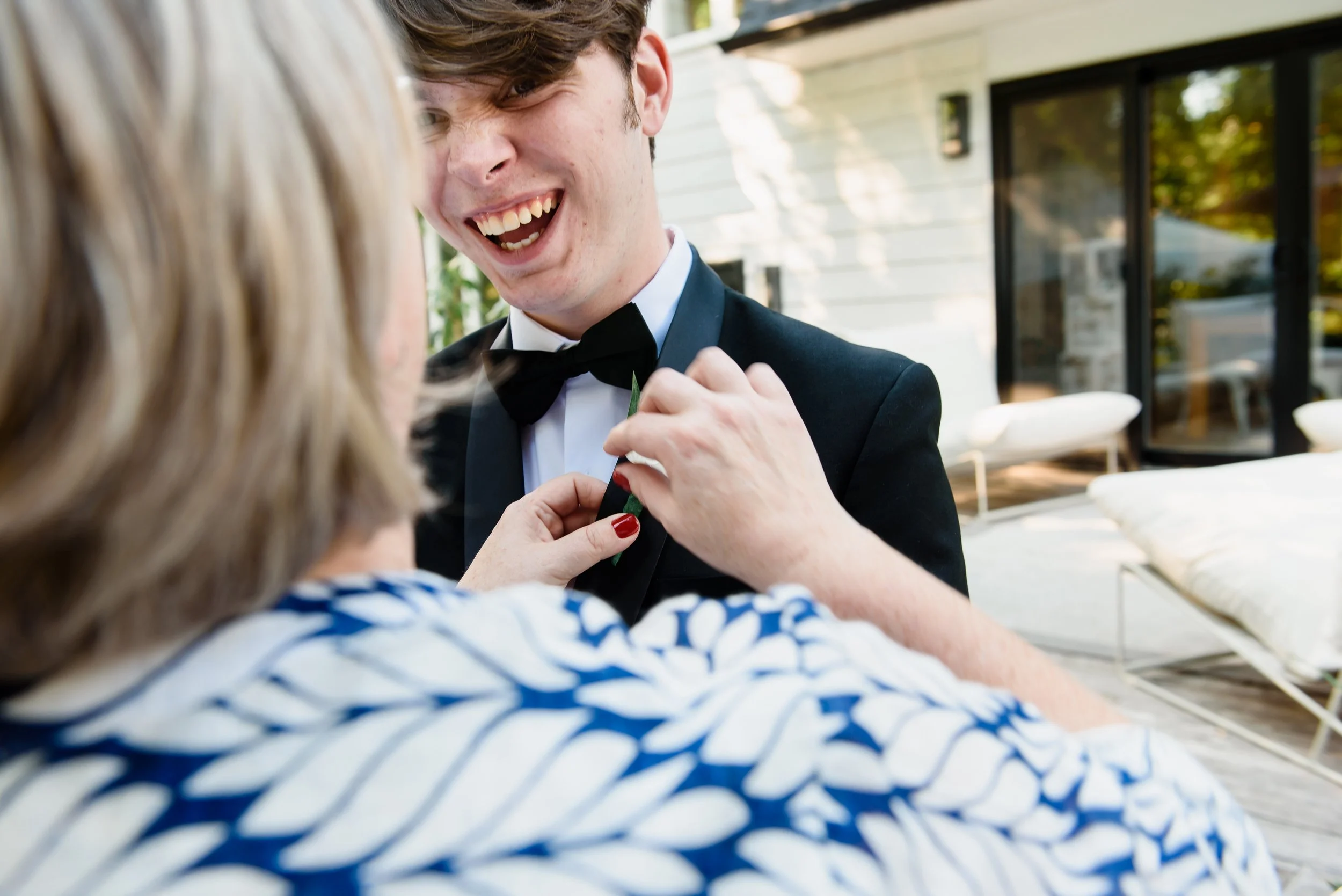 Woman places corsage on lapel of laughing young boy's tuxedo.